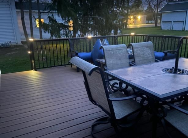 Outdoor deck with dining set and railing with lights at dusk.