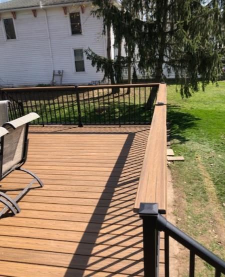 Wooden deck with black railings overlooking a grassy yard, near a white building.