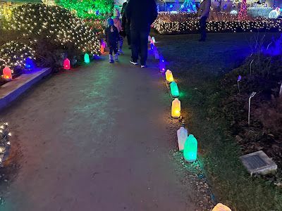 Path lined with colorful glowing lights, people walking on path, holiday decorations.
