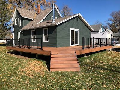 Green house with a brown deck, black railings, and a blue sky.