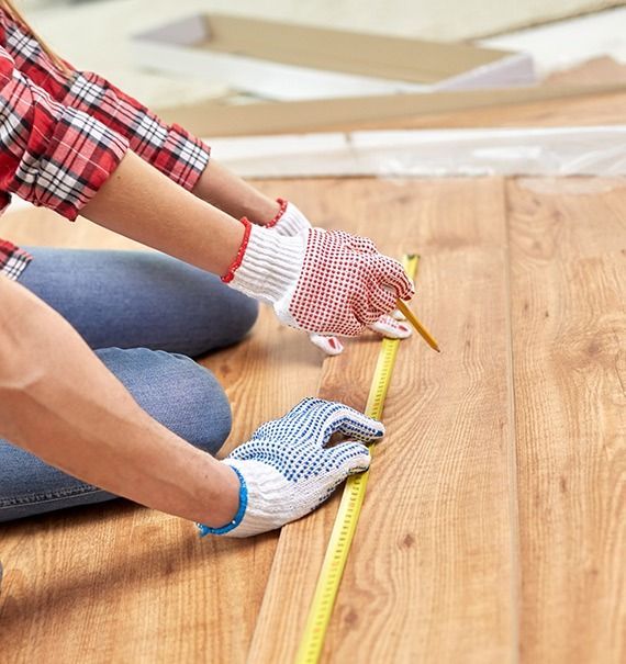 A person is measuring a wooden floor with a tape measure.