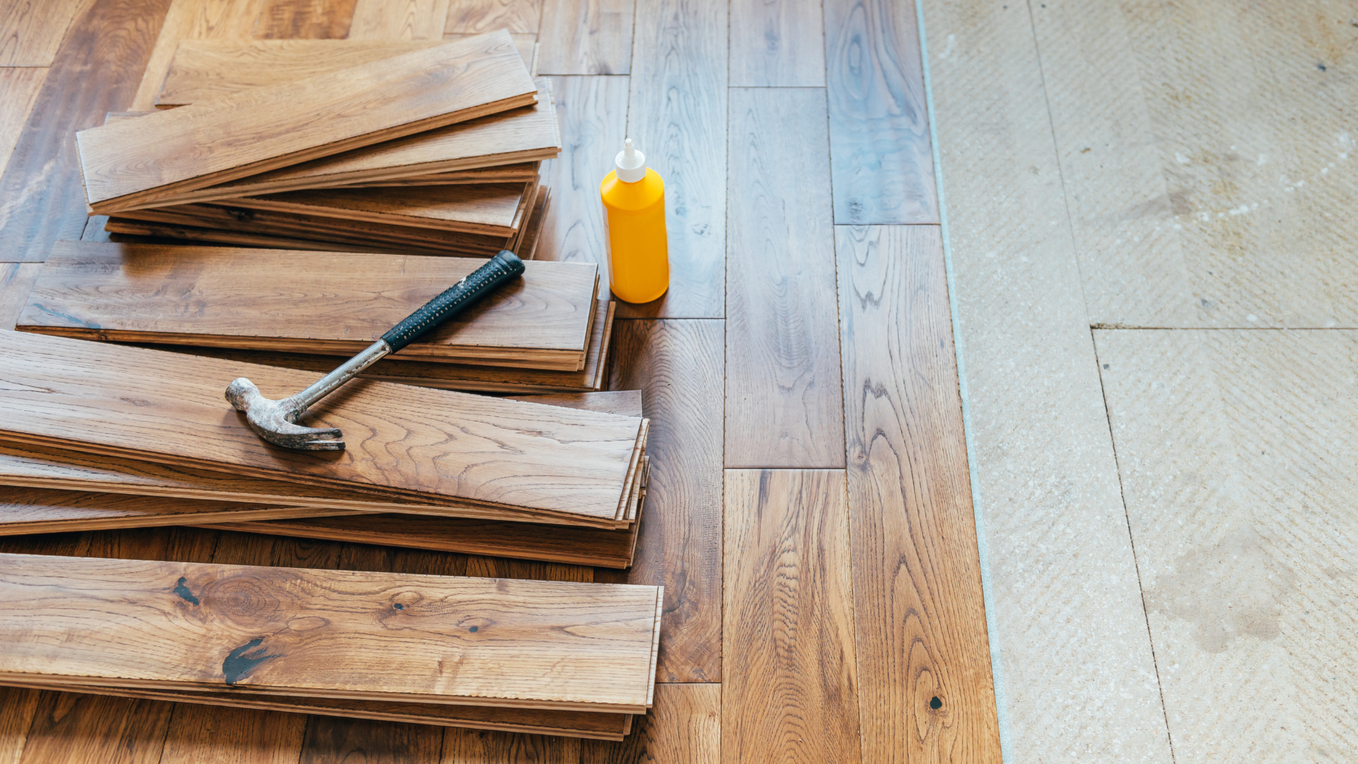 A hammer and a bottle of glue are sitting on a wooden floor.