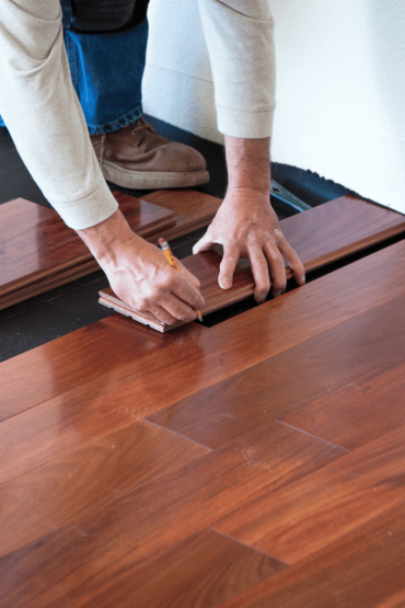A person is measuring a piece of wood on the floor