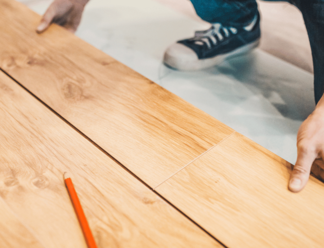 A person is measuring a piece of wood with a pencil.