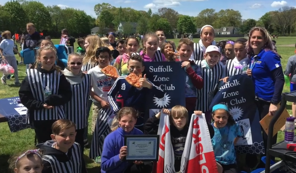 Group holding club banners and a certificate outdoors in a park, smiling for a team photo