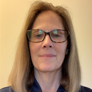 Portrait of a person wearing glasses and a dark blue shirt against a light wall