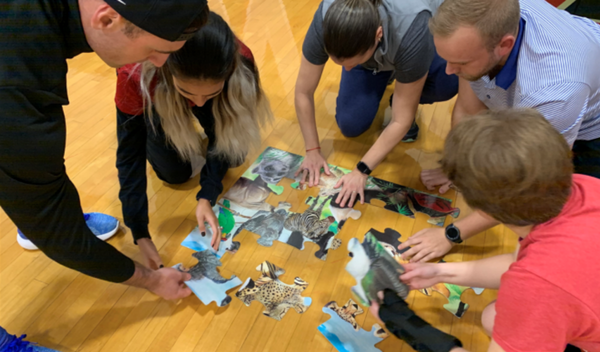 Group of people crouching on a wooden floor, assembling a jigsaw puzzle together