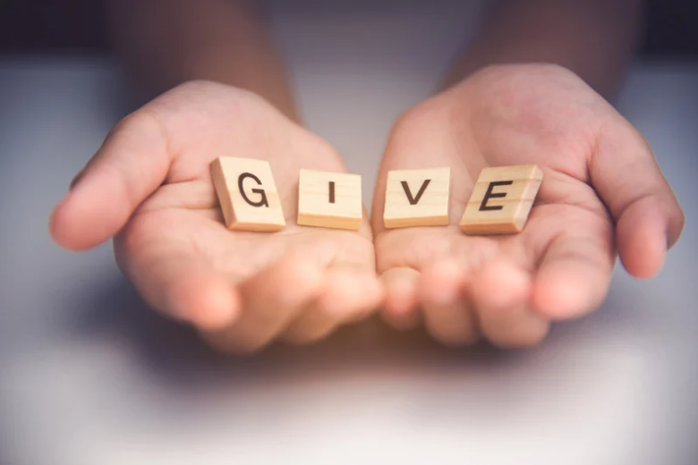 Hands holding wooden blocks spelling “GIVE” on a blurred background.