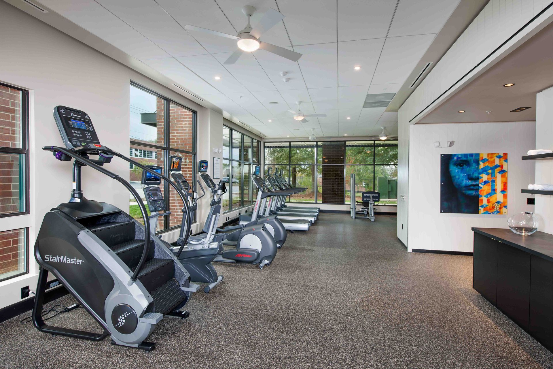 A gym with a lot of exercise equipment and a ceiling fan.