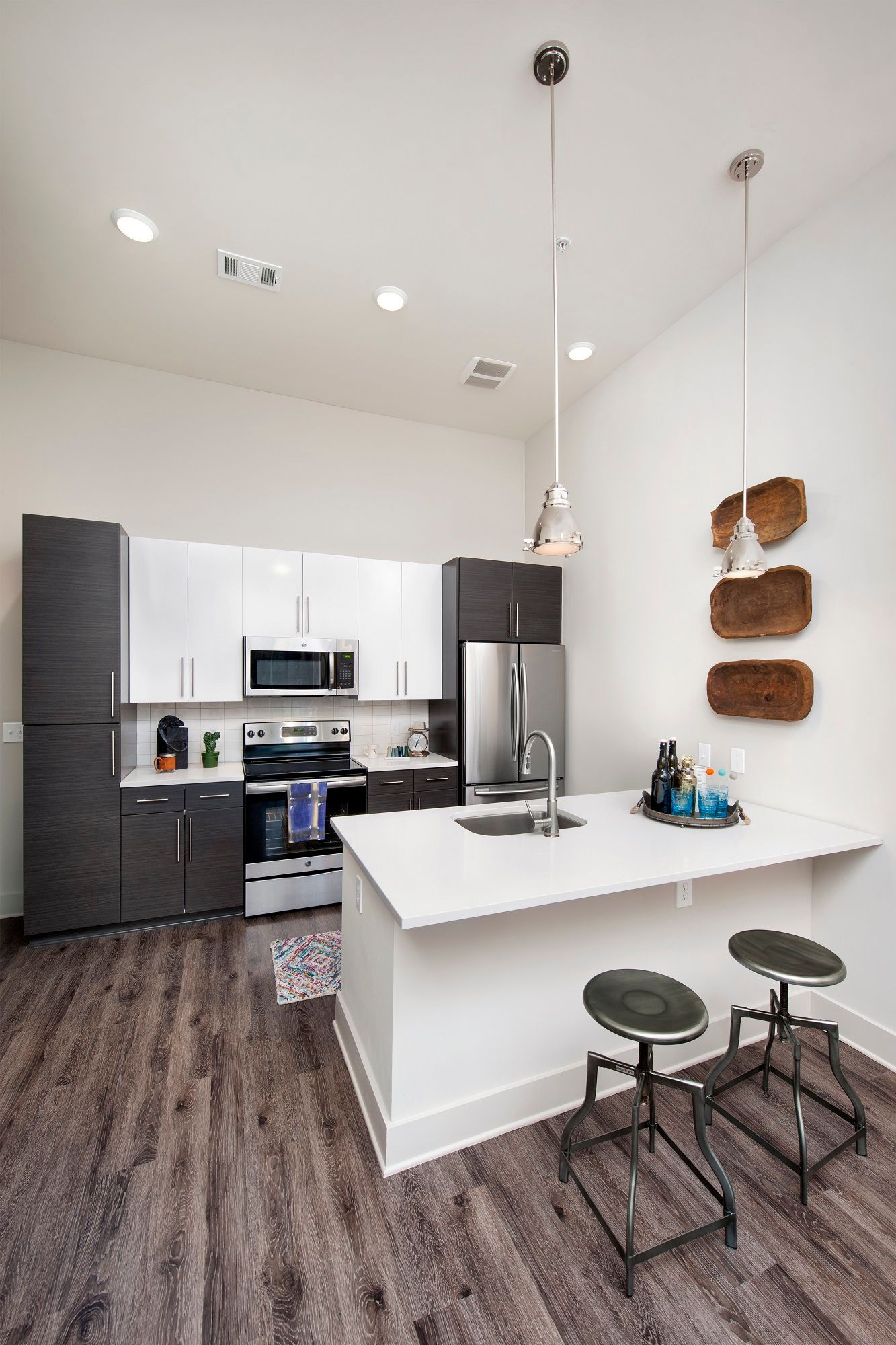 A kitchen with stools, a sink, a refrigerator, and a microwave.