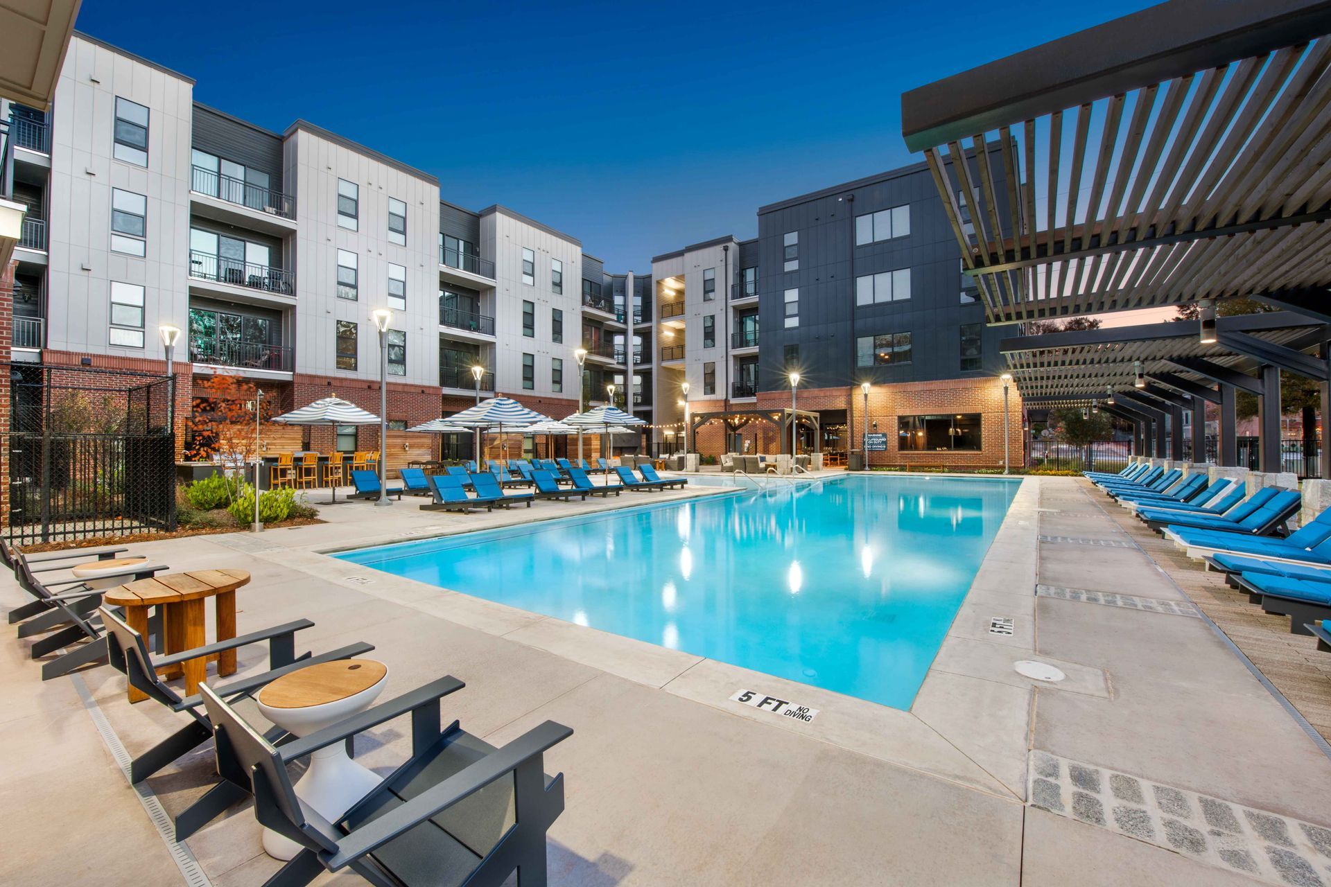 A large swimming pool surrounded by chairs and umbrellas in front of a building.