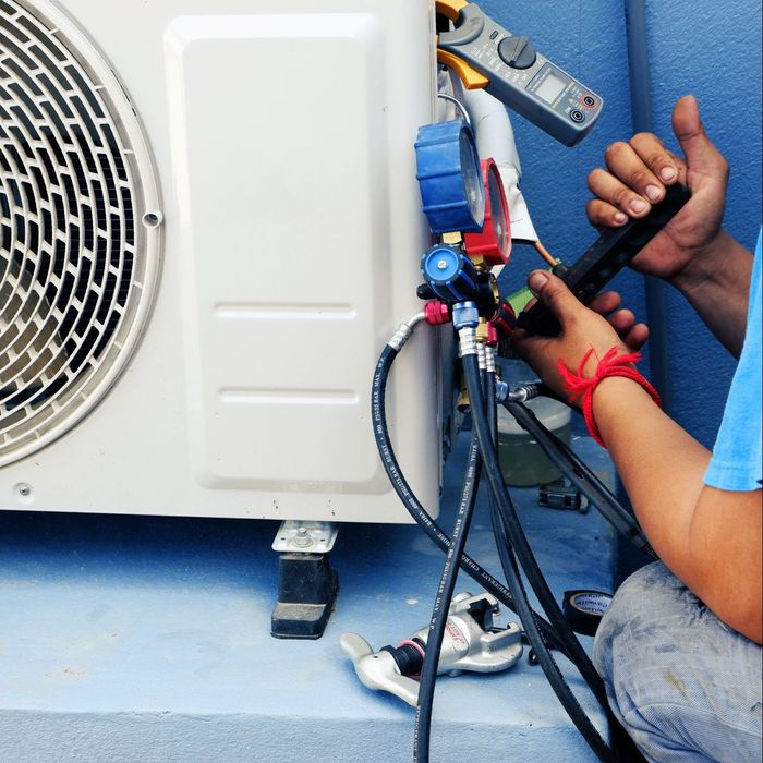 A man is working on an air conditioner with a pair of pliers