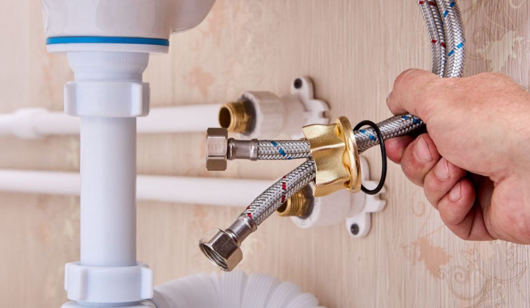 Plumber connecting chrome pipes under a sink with a wrench on a wooden wall panel