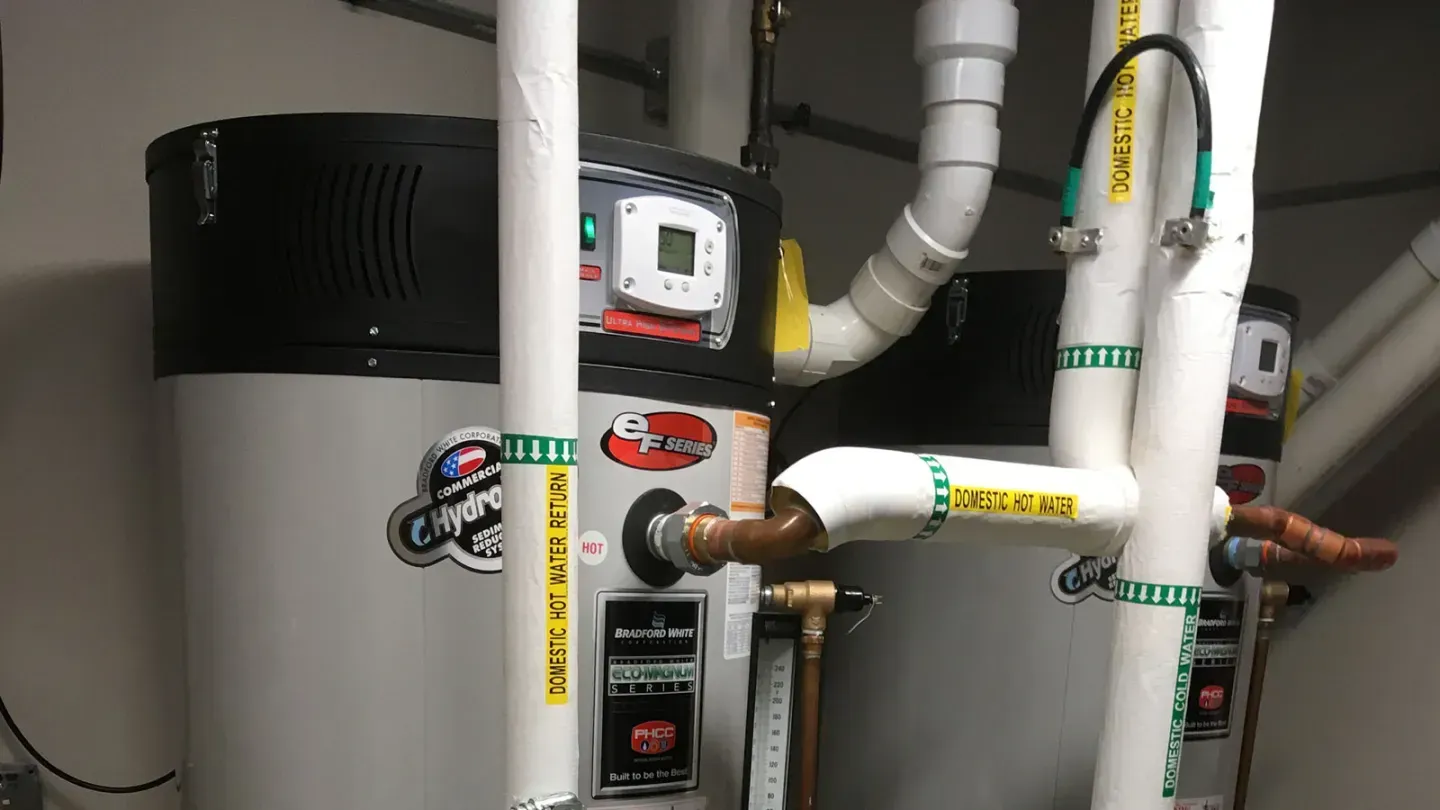 Water heater and plumbing pipes with valves in a utility closet.