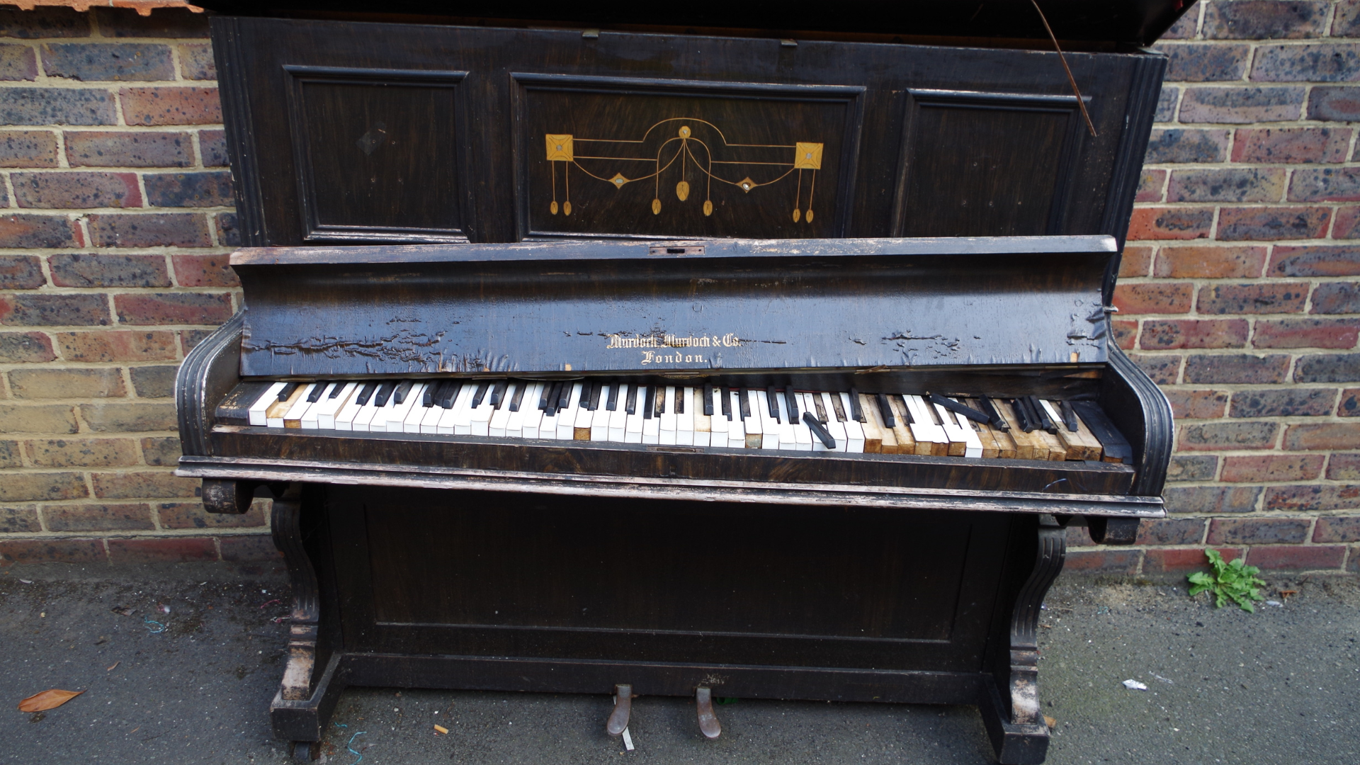 An old piano is sitting in front of a brick wall