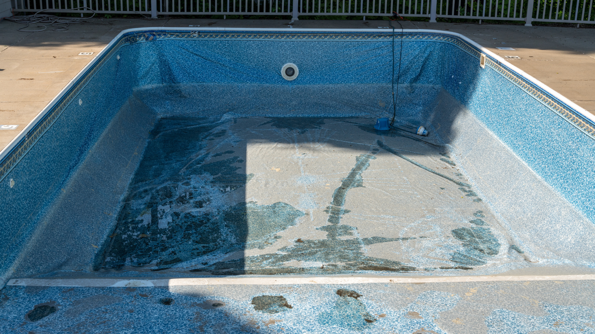 An empty swimming pool is sitting on the ground next to a fence.