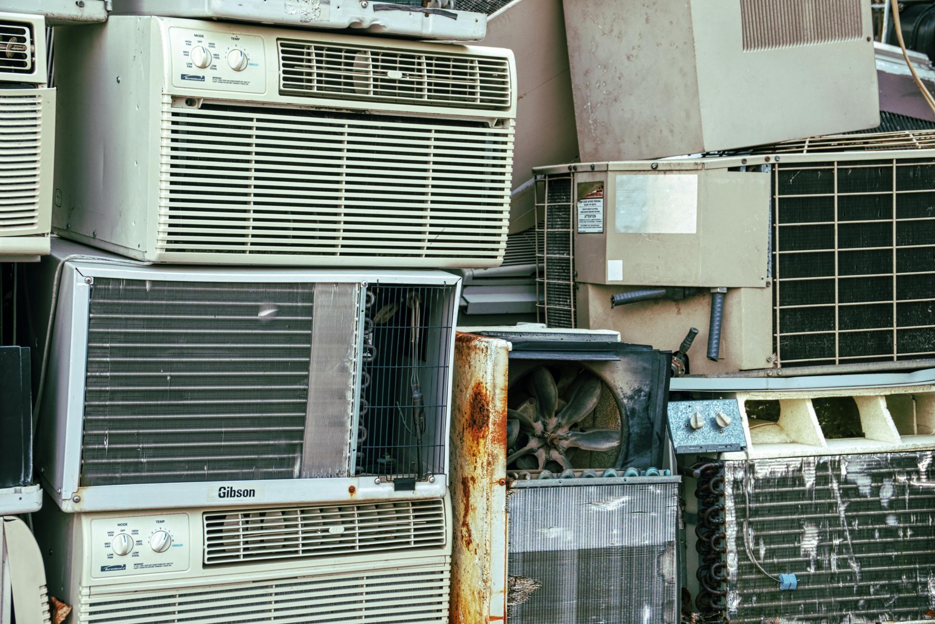 Pile of discarded air conditioners, various sizes and conditions, outdoors.