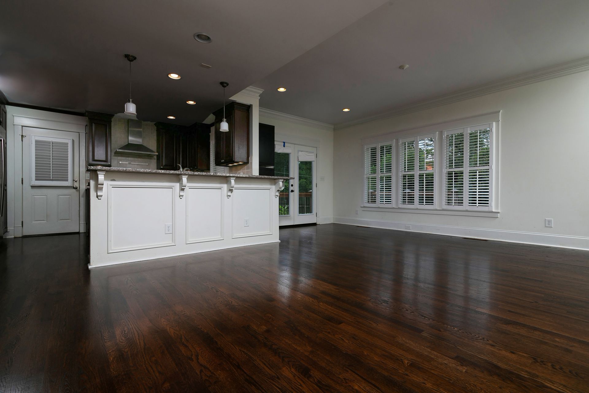 A large empty room with hardwood floors and a kitchen in the background.
