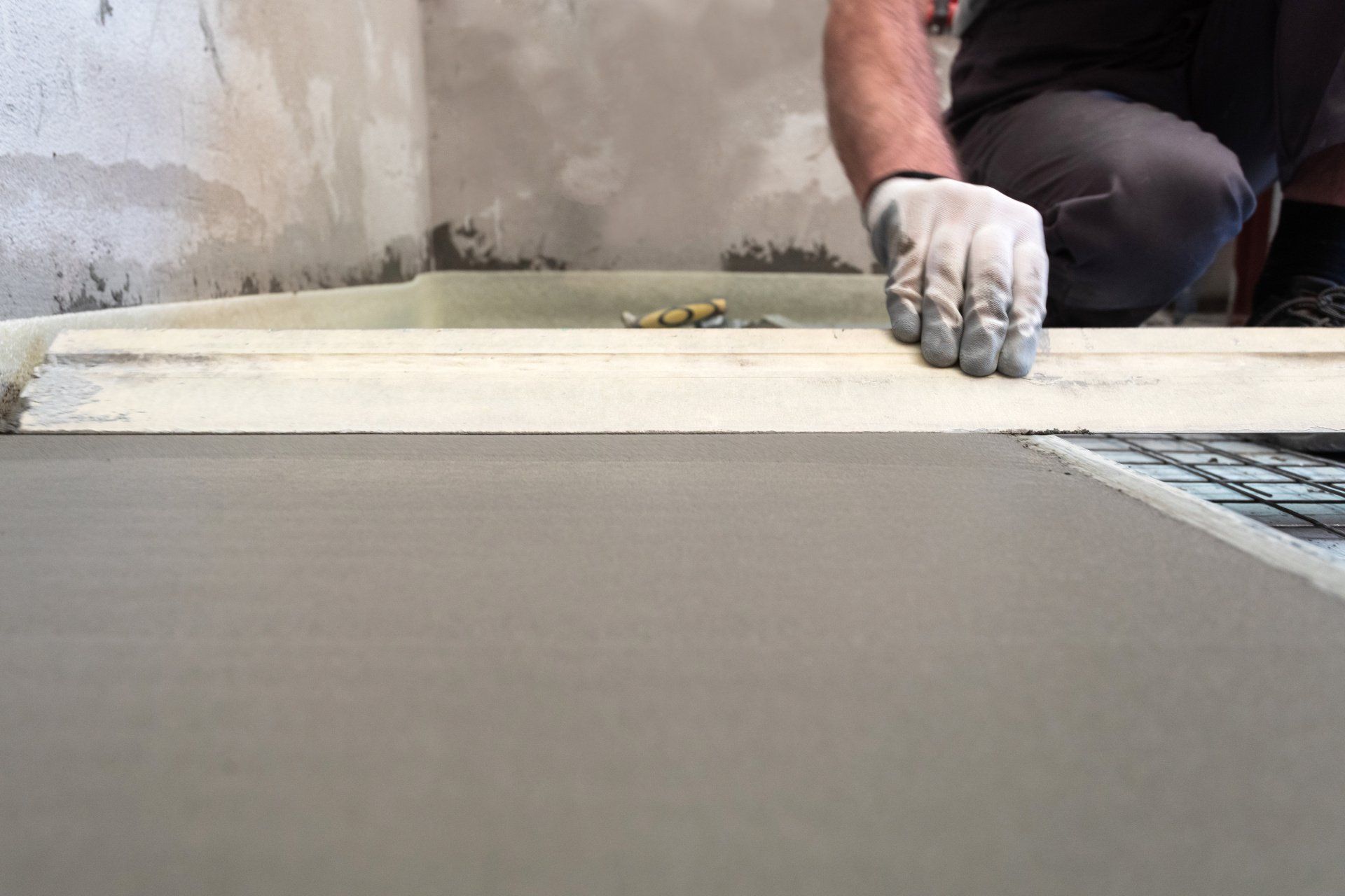 A man is laying concrete on the floor in a room.