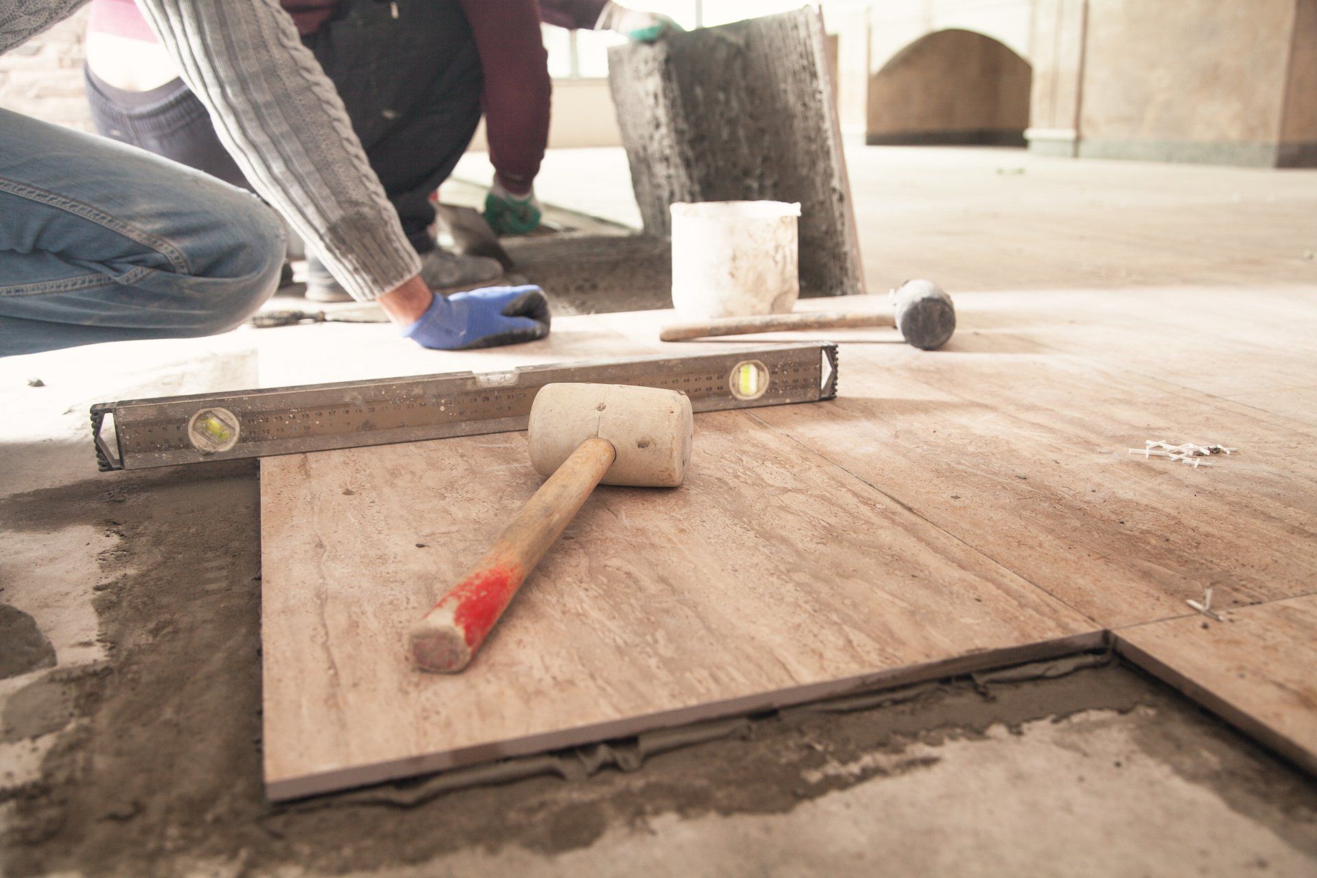 A person is laying tiles on the floor with a hammer and a level.