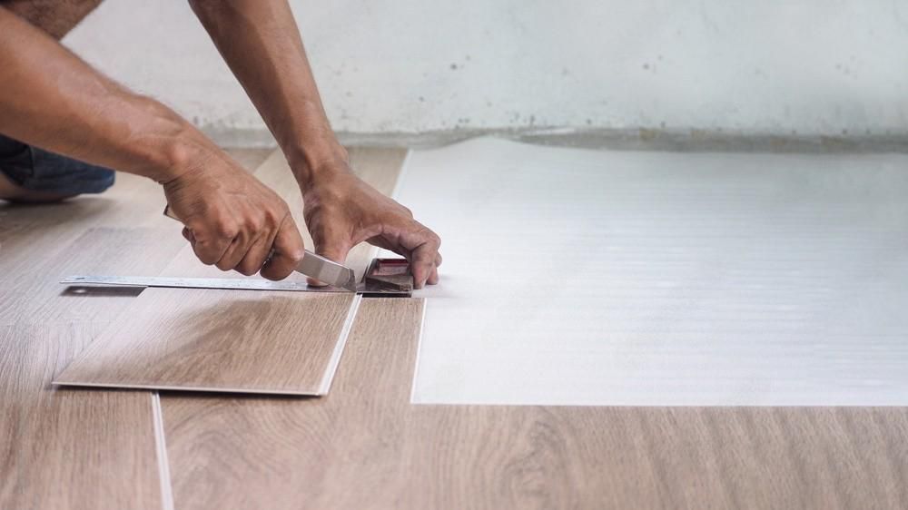 a man is cutting a piece of vinyl flooring with a pair of scissors .
