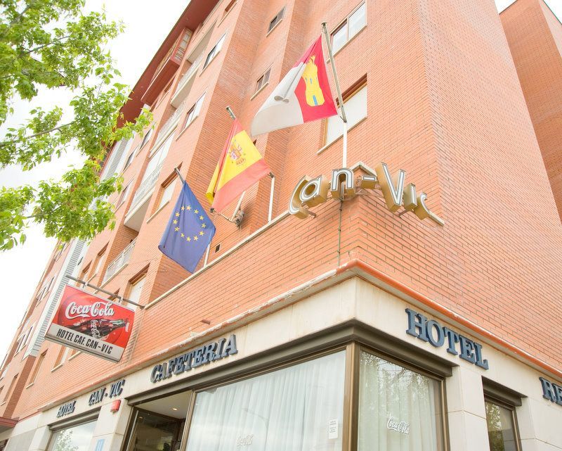 Fachada de hotel en un edificio de ladrillo con banderas españolas y de la UE y un letrero de Coca-Cola sobre la entrada.