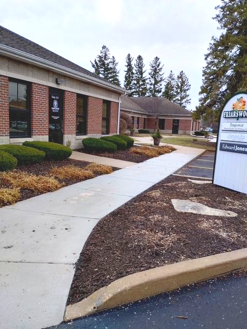 Insurance agency exterior, blue sign above entrance, brick and blue siding, two parked cars.