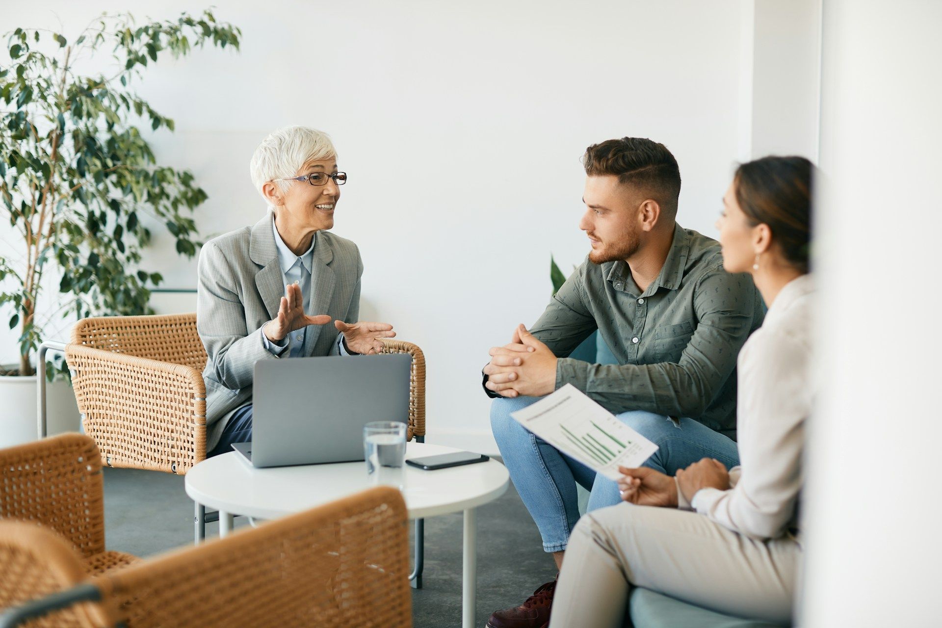 A woman is talking to a man and a woman while sitting at a table with a laptop.