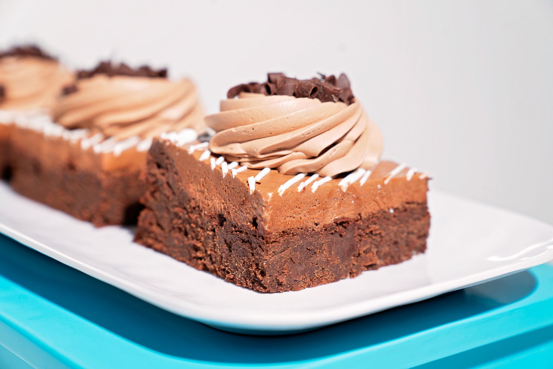 A close up of a brownie with chocolate frosting on a white plate.