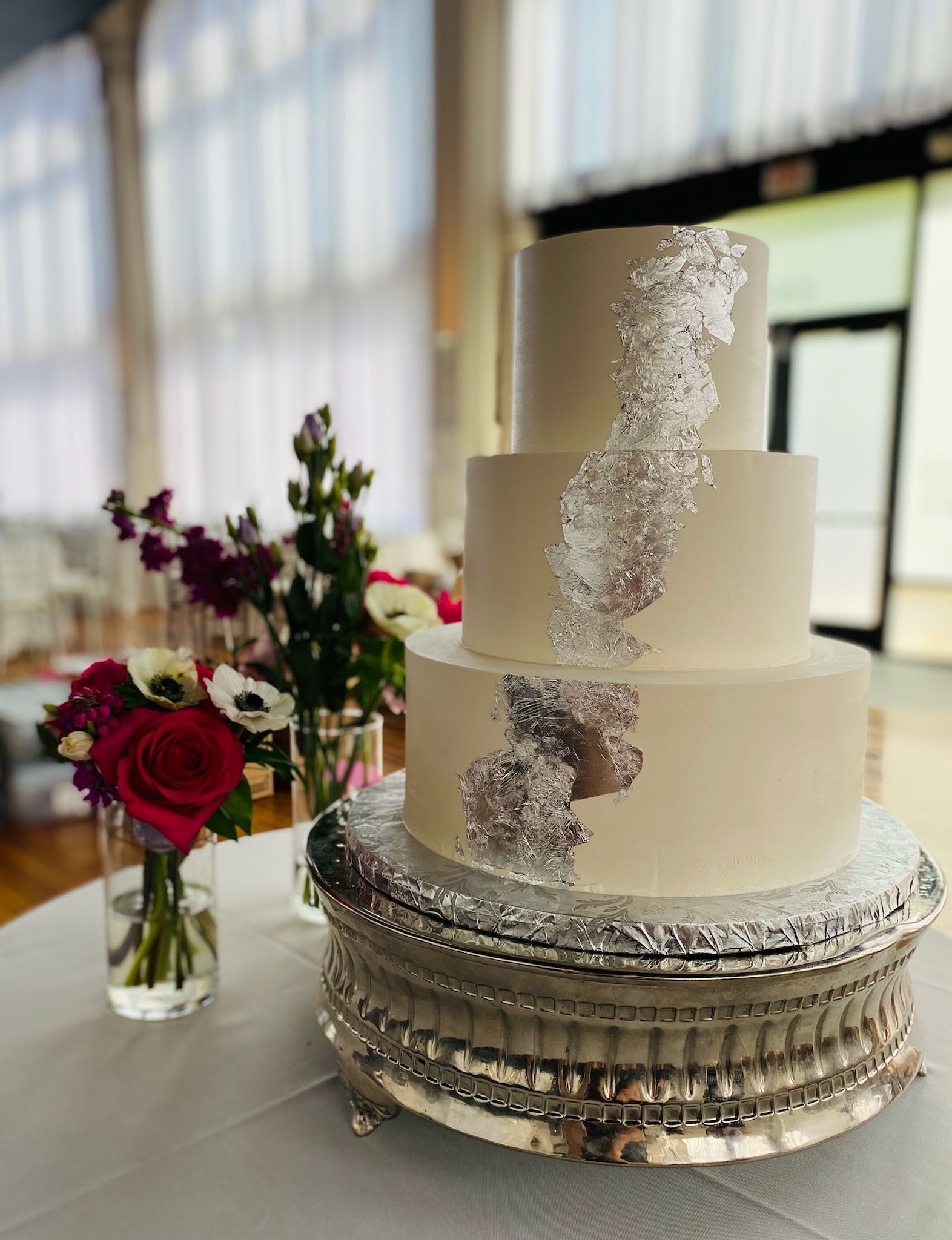 A wedding cake is sitting on top of a silver cake stand on a table.