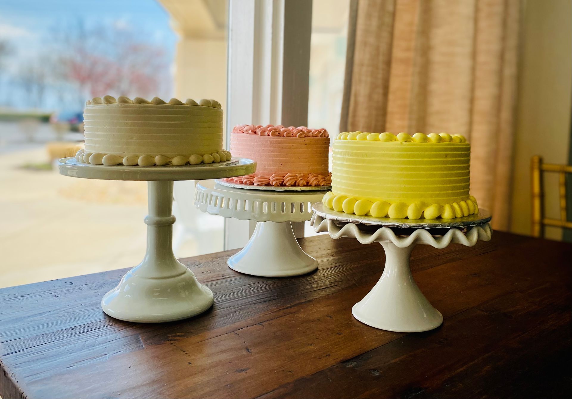 Three cakes are sitting on a wooden table in front of a window.