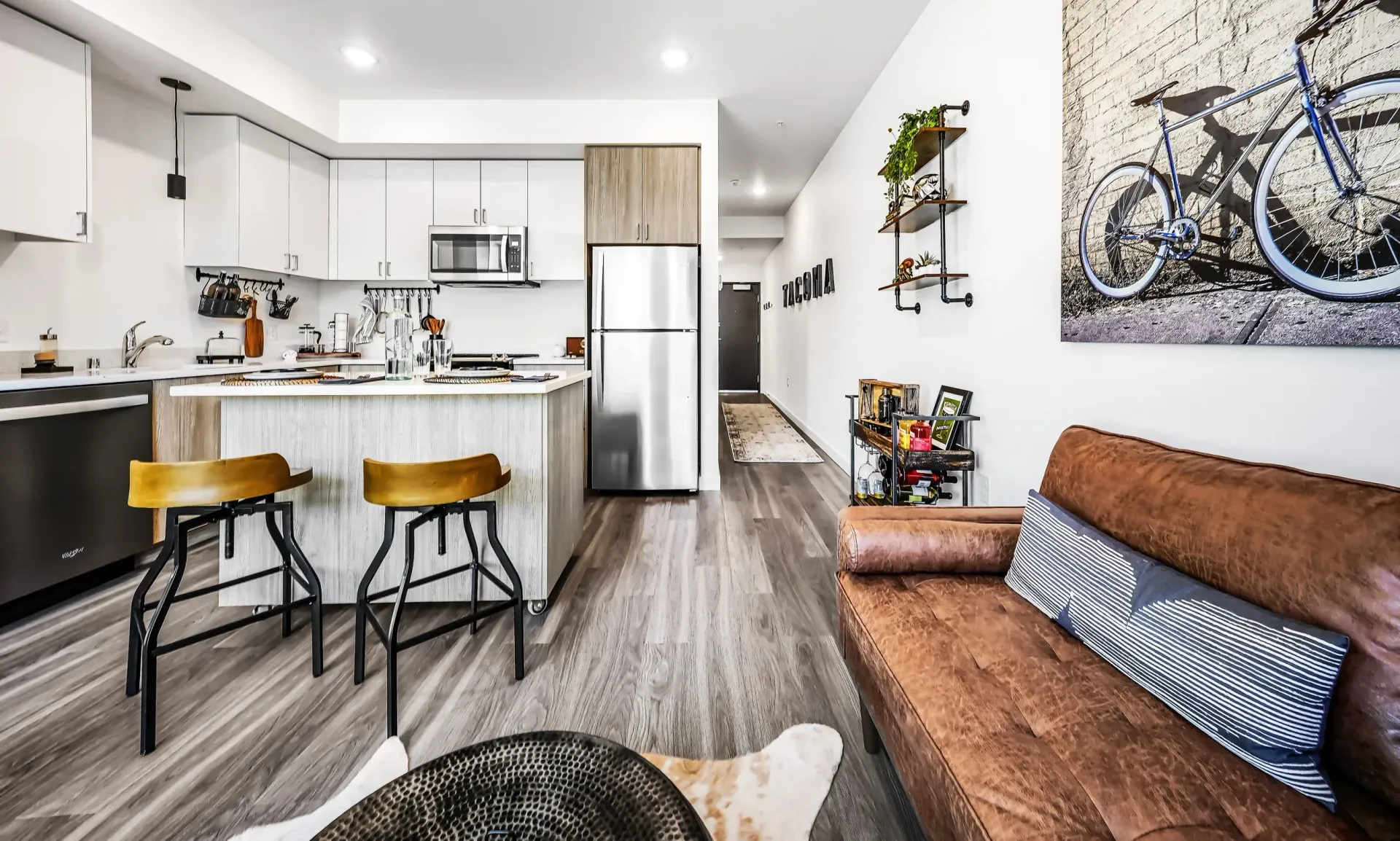 Modern apartment interior with kitchen island, stainless steel appliances, and brown leather sofa at The Lex in Tacoma, WA.