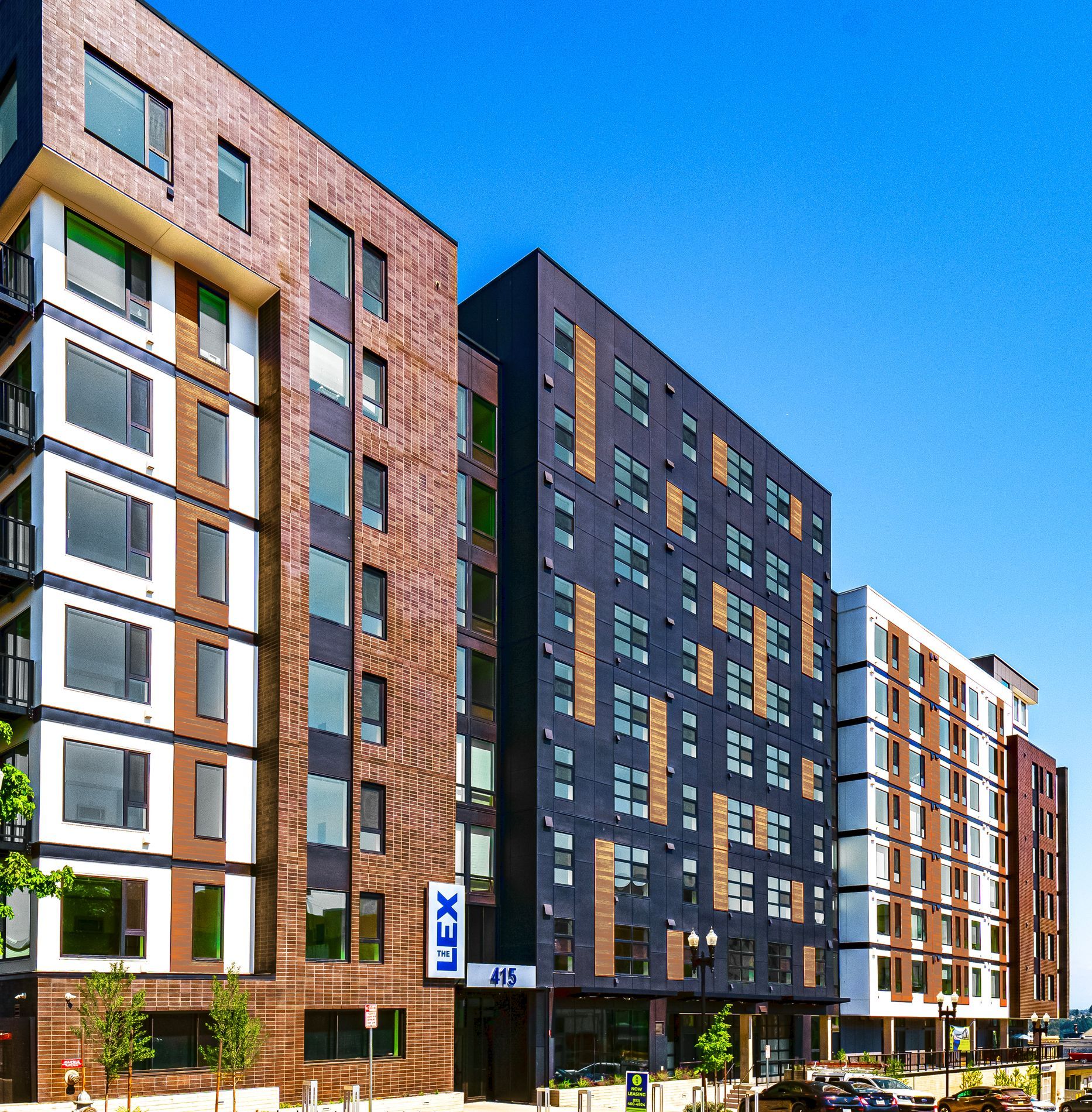 Modern apartment buildings with brick, brown, and white exteriors against a blue sky at The Lex in Tacoma, WA.