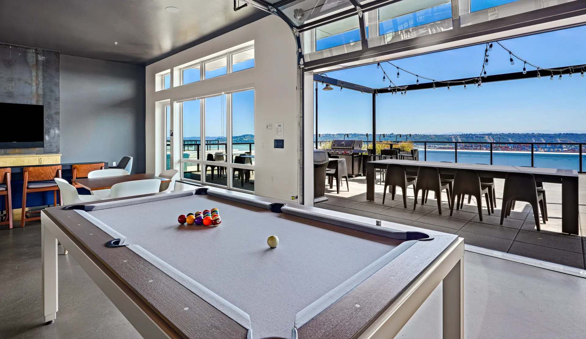 Pool table in a room with a large open doorway leading to an outdoor deck with a view of the water at The Lex in Tacoma, WA.