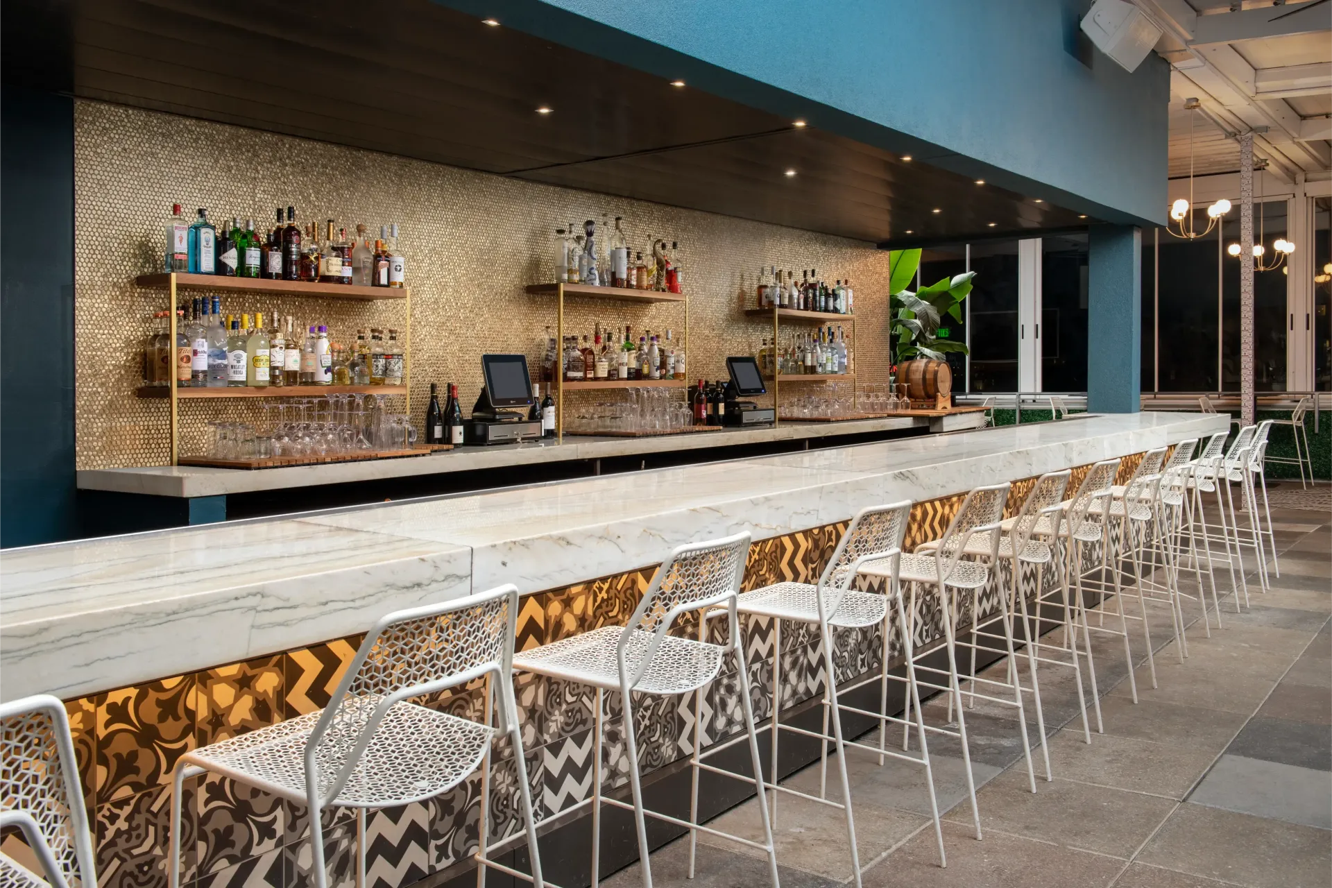 A long bar with a lot of stools and shelves filled with alcohol.