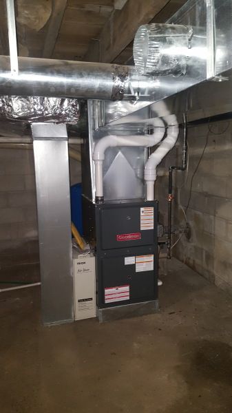 Furnace and ductwork in a basement. Grey metal unit with white pipes and air vents on a concrete floor.