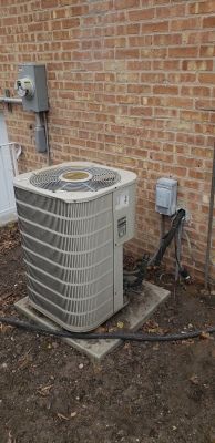 An air conditioning unit against a brick wall. Electrical boxes are mounted above.