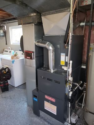 Furnace and ductwork in a basement laundry room. Gray furnace with silver ductwork, next to a white washing machine.