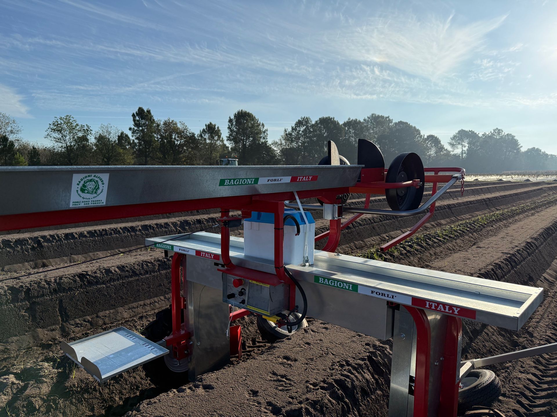 Una mietitrice agricola in metallo si trova in un campo arato sotto un cielo azzurro e soleggiato.