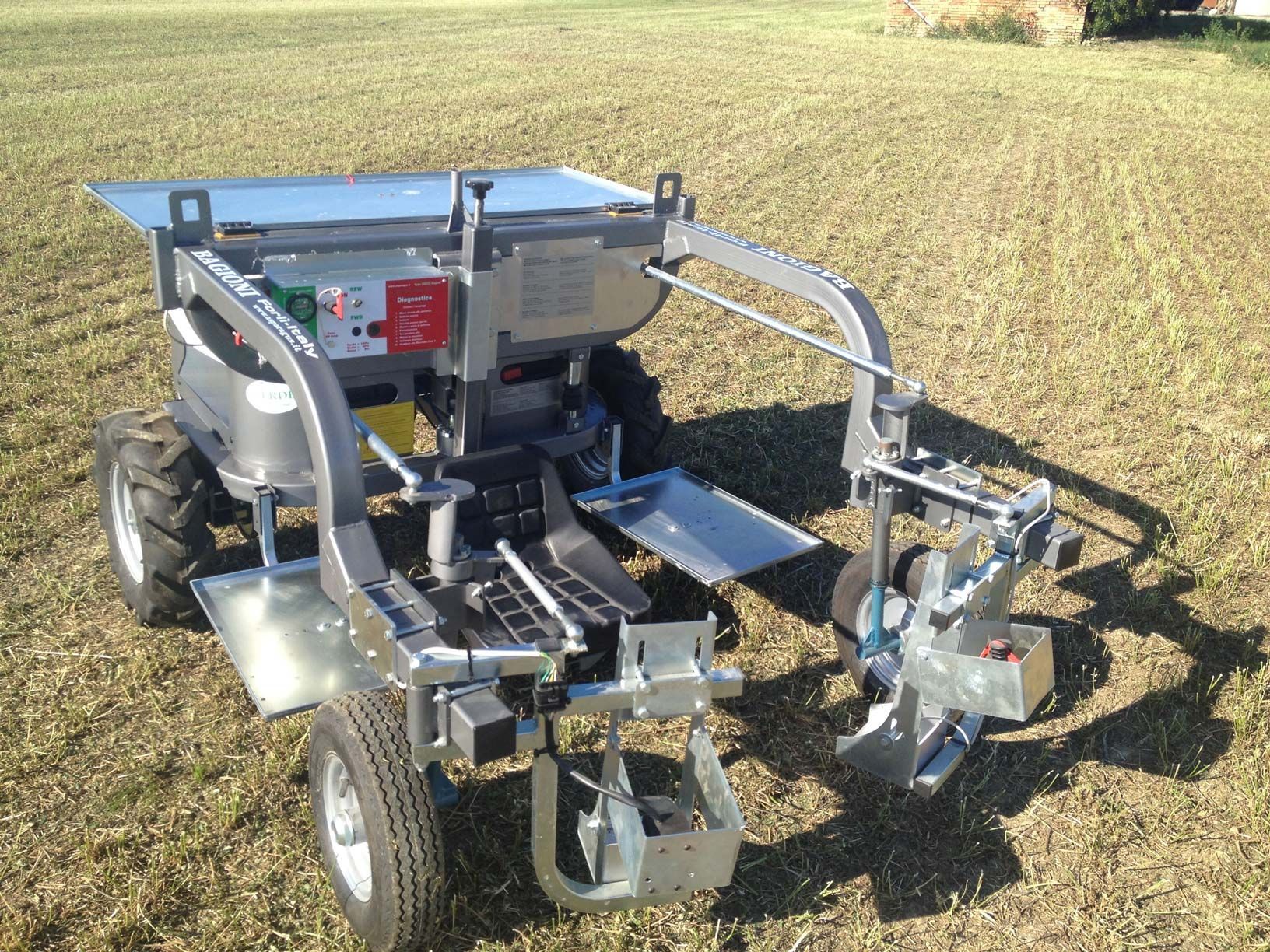 Un robot agricolo metallico e automatizzato, utilizzato per diserbare o raccogliere, si erge su un campo pianeggiante e già mietuto.