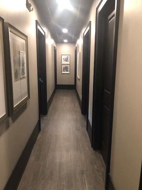 Narrow hallway with dark doors and trim, art on the walls, and recessed lighting.
