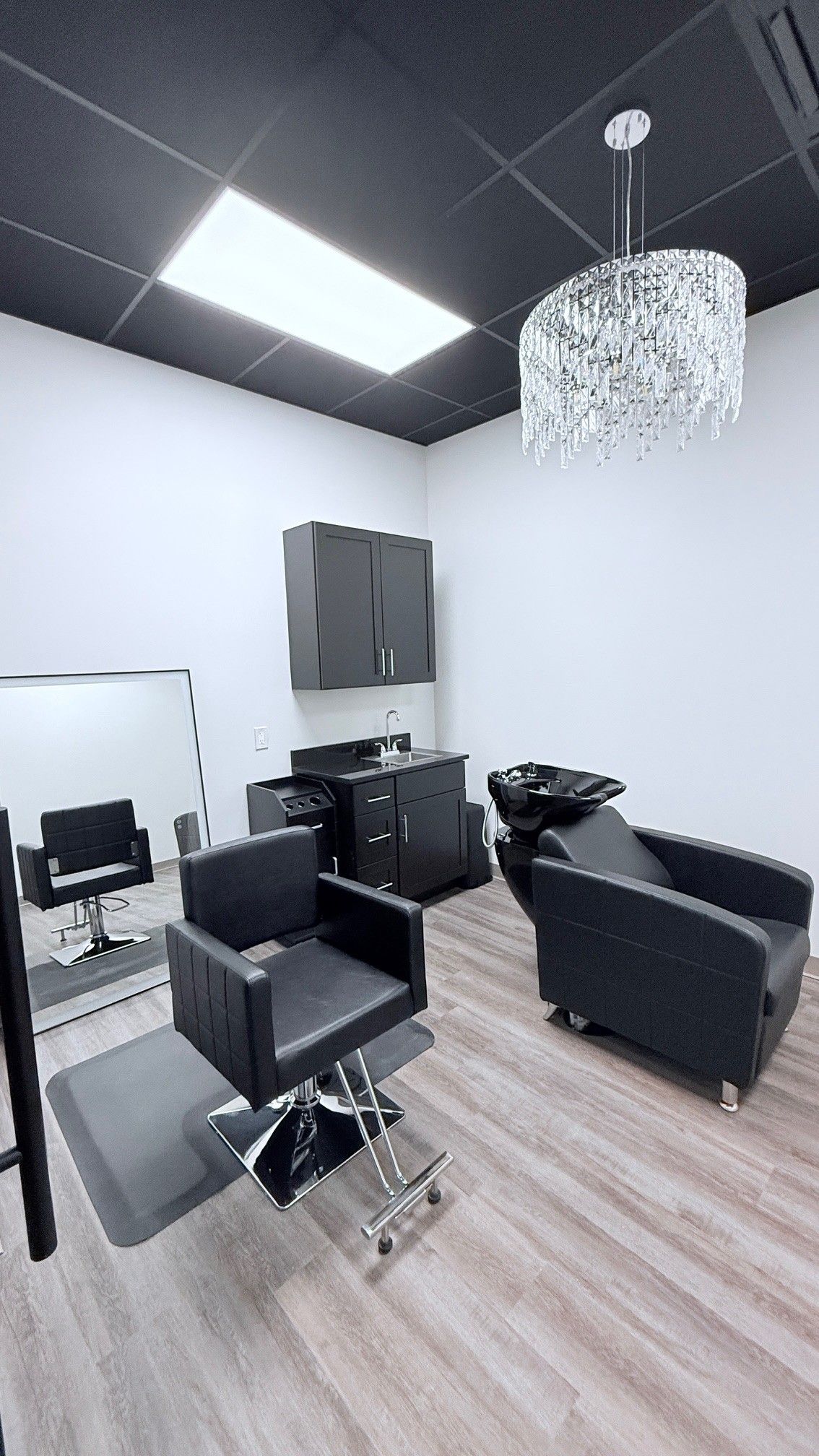 Hair salon interior with black chairs, sink, mirror, and chandelier.