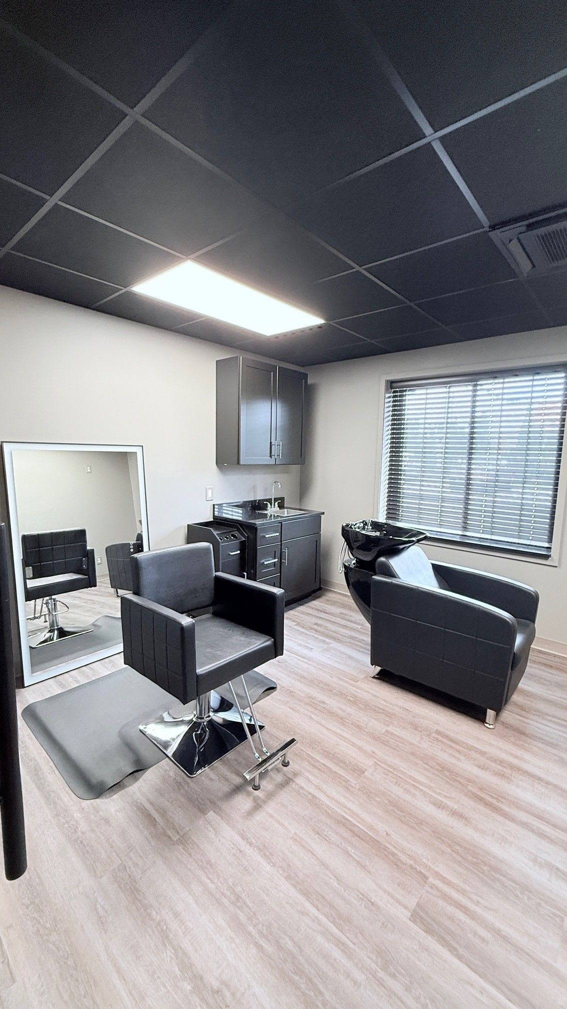 Hair salon interior with black chairs, cabinets, a large mirror, and light-colored wood flooring.