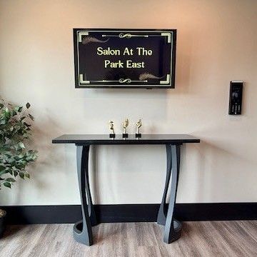 Reception area with a TV screen and table, Salon At The Park East, with decor and a plant.