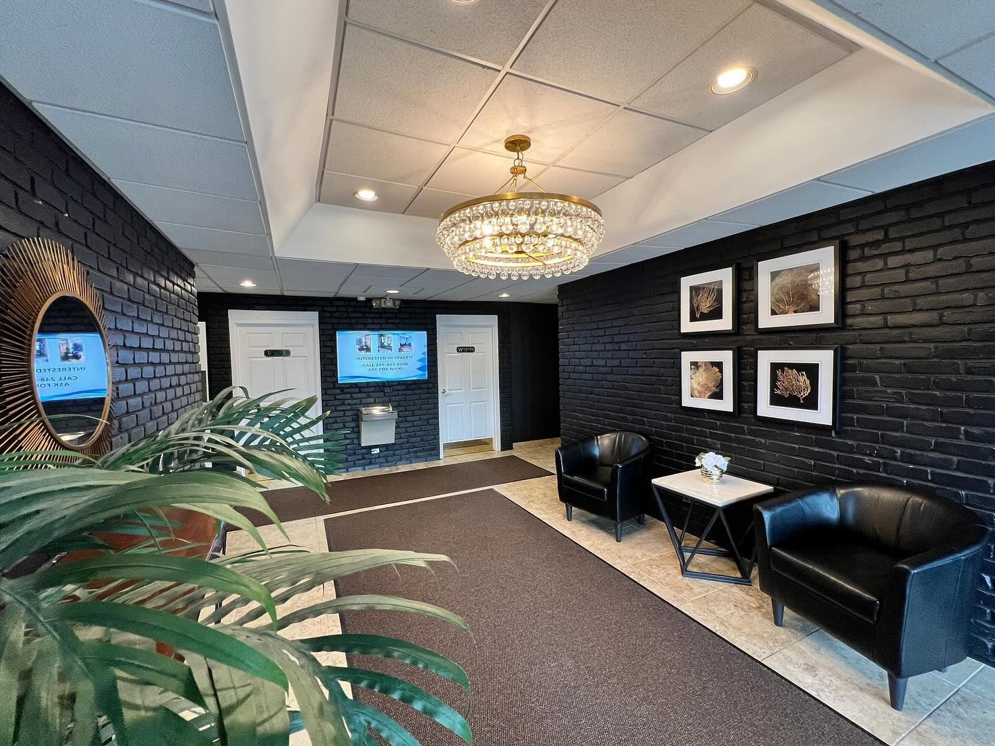 Lobby with black brick walls, chandelier, seating, and a TV screen.