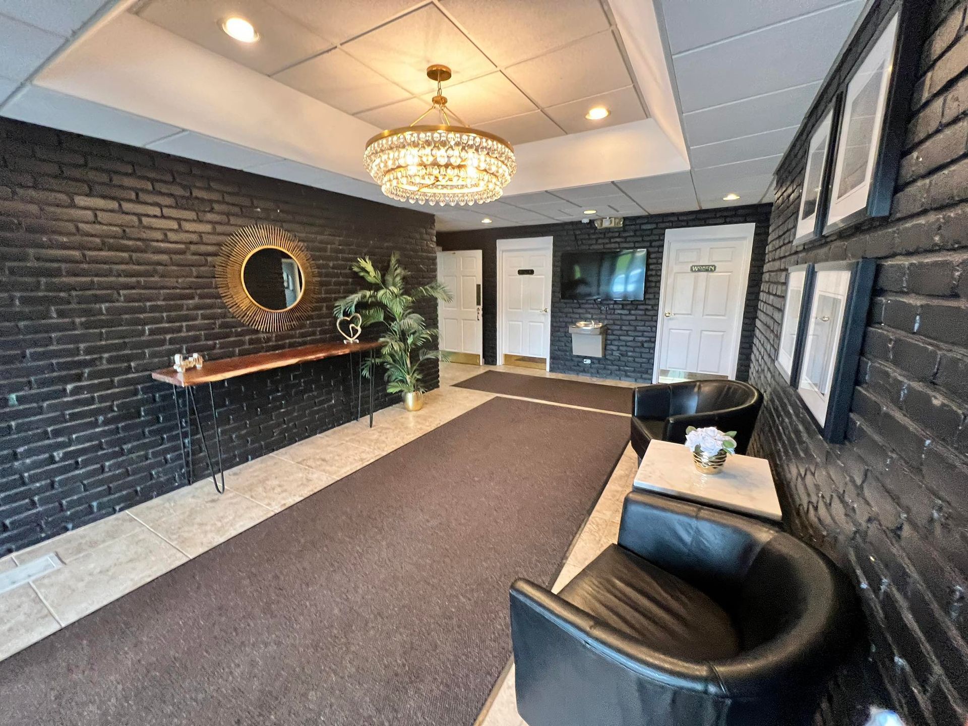 Black brick wall entryway with chandelier, two black chairs, and a long table.
