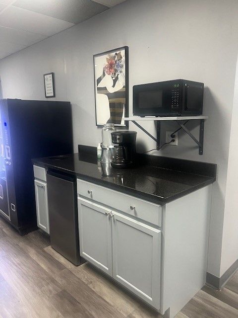 Kitchenette with microwave, coffee maker, cabinets, vending machine. Gray and white color scheme.