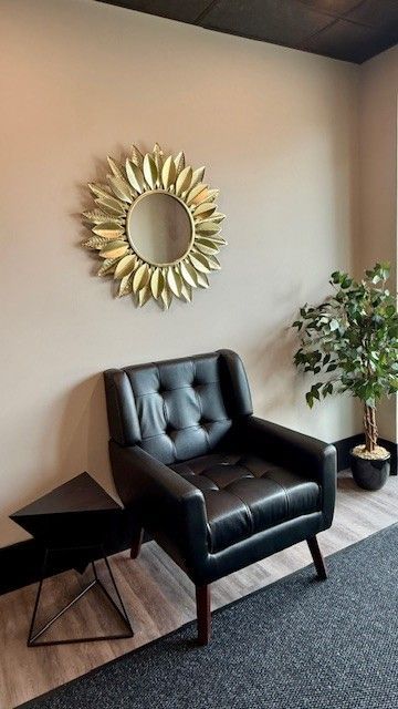 Black leather armchair, gold mirror, black side table, potted plant against a beige wall.