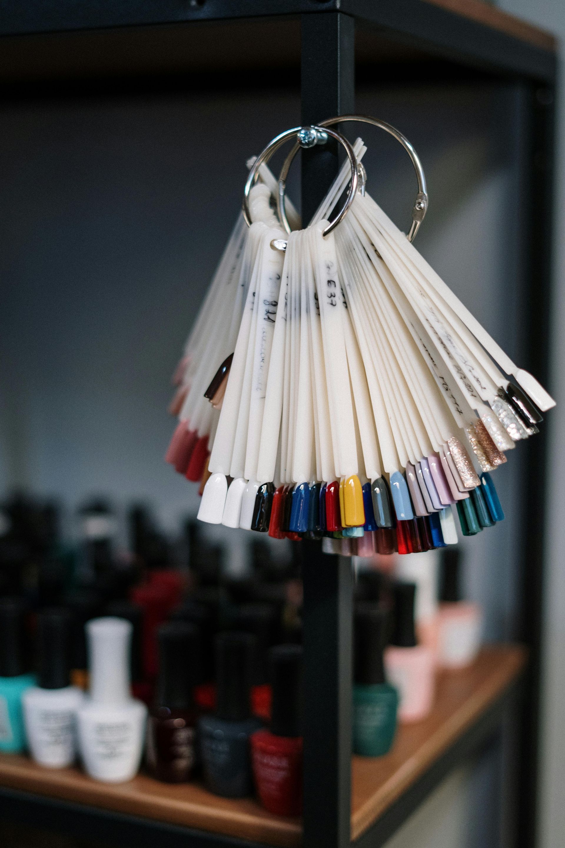 Nail polish color samples fanned on a ring, with bottles of polish in the background on a shelf.