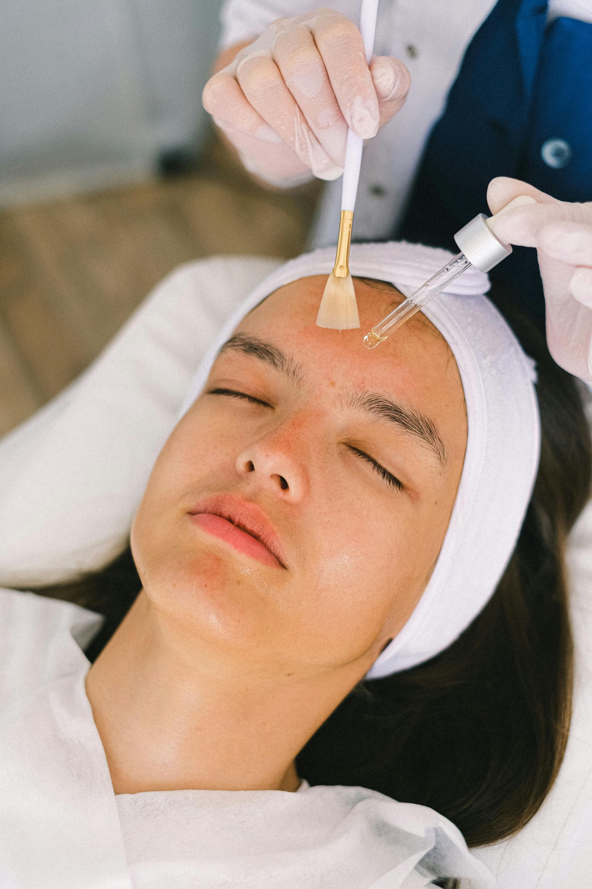 Person receiving a facial peel treatment. Esthetician applies product to forehead.